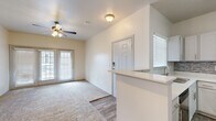 This single-floor residence offers a practical and comfortable layout with two bedrooms and two bathrooms. The open living area is bright and inviting, featuring plush carpeting, a ceiling fan, and sliding glass doors that welcome natural light and provide outdoor access. The kitchen is well-equipped with white shaker-style cabinetry, a mosaic tile backsplash, stainless steel appliances including an electric range, microwave, and dishwasher, and a light stone countertop that extends to a peninsula with a sink — seamlessly connecting the kitchen to the entry and living areas. Wood-look flooring runs throughout the kitchen and bathrooms, offering a clean contrast to the carpeted rooms. The primary bedroom is generously sized, featuring a ceiling fan, a large window with natural light, and access to a walk-in closet. The second bedroom also includes a ceiling fan and a sizable window. Both bathrooms share a consistent design with white vanities, stone countertops, wood-look flooring, and tiled shower-tub combinations accented by a decorative mosaic border. A hallway connects the bedrooms to the rest of the home, and a dedicated utility room and closet round out the space, offering practical storage and functional living solutions throughout.