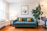 Located at 2 Spruce St in Dover, NJ, this single-floor residence offers a thoughtfully designed layout that balances comfort and modern functionality. Throughout the space, warm-toned hardwood flooring provides a cohesive and inviting foundation.

The living area is bright and welcoming, featuring a window with blinds that allows natural light to fill the room. A teal mid-century modern sofa anchors the space, complemented by a round gold accent table, a stylish floor lamp, and curated wall art, creating a relaxed yet refined atmosphere.

The kitchen is designed with efficiency and style in mind. It features contemporary flat-front cabinetry in a warm gray-wood finish, white quartz countertops, a stainless steel undermount sink, and stainless steel appliances including an electric range and built-in microwave. Clean white walls and continued hardwood flooring keep the space bright and cohesive.

The bedroom is a calm retreat, finished in soft blue-gray tones that promote rest and relaxation. It accommodates a full-size bed with an elegant metal headboard and is flanked by matching nightstands with lamps. Two sets of double closet doors provide ample storage.

The bathroom is clean and modern, featuring a wood-tone vanity with white countertop, a large mirror, tile flooring, and a glass-enclosed shower, delivering a spa-like experience within a practical layout.
