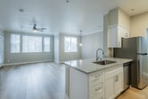 This single-floor unit offers a thoughtfully designed open-concept layout that seamlessly connects the kitchen and living area. The kitchen is outfitted with white shaker cabinetry, granite countertops, stainless steel appliances including a range and microwave, and a peninsula with an undermount sink and pendant lighting above — ideal for both meal preparation and casual dining. The living area is generously proportioned, featuring light hardwood-style flooring, crown molding, a ceiling fan, and multiple windows with vertical blinds that allow abundant natural light and views of surrounding greenery.

The bedroom is carpeted and well-sized, accompanied by a spacious walk-in closet with multi-tier wire shelving systems that maximize storage. A second walk-in closet provides additional storage capacity. Two full bathrooms mirror each other in design, each featuring a tub-shower combo, white vanity cabinetry with granite countertops, brushed nickel hardware, and hardwood-style flooring. One bathroom includes accessibility grab bars near the tub. A dedicated laundry area houses a top-load washer with overhead cabinetry, adding everyday convenience. The neutral warm-beige and white color palette throughout the unit creates a clean, cohesive, and welcoming atmosphere.