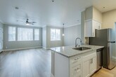This single-floor unit offers a thoughtfully designed open-concept layout that seamlessly connects the kitchen and living area. The kitchen is outfitted with white shaker cabinetry, granite countertops, stainless steel appliances including a range and microwave, and a peninsula with an undermount sink and pendant lighting above — ideal for both meal preparation and casual dining. The living area is generously proportioned, featuring light hardwood-style flooring, crown molding, a ceiling fan, and multiple windows with vertical blinds that allow abundant natural light and views of surrounding greenery.

The bedroom is carpeted and well-sized, accompanied by a spacious walk-in closet with multi-tier wire shelving systems that maximize storage. A second walk-in closet provides additional storage capacity. Two full bathrooms mirror each other in design, each featuring a tub-shower combo, white vanity cabinetry with granite countertops, brushed nickel hardware, and hardwood-style flooring. One bathroom includes accessibility grab bars near the tub. A dedicated laundry area houses a top-load washer with overhead cabinetry, adding everyday convenience. The neutral warm-beige and white color palette throughout the unit creates a clean, cohesive, and welcoming atmosphere.