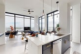 Located at 615 E Morehead St in the heart of Charlotte, NC, this thoughtfully designed 2-bedroom, 2-bathroom residence offers a seamless blend of modern aesthetics and functional living across a single floor. Dramatic floor-to-ceiling windows dominate the open-concept kitchen and living area, flooding the space with natural light and framing sweeping views of the Charlotte skyline. The kitchen is outfitted with slate-blue cabinetry accented by gold hardware, stainless steel appliances, and a generous waterfall island with bar seating — ideal for both everyday living and entertaining. Pendant lighting adds a refined touch overhead. The living and dining areas extend naturally from the kitchen, benefiting from the same expansive glazing and light hardwood flooring throughout. The spacious primary bedroom continues the floor-to-ceiling window theme, offering direct city views, while the second bedroom is equally well-lit with its own large window. Both bathrooms feature sleek, contemporary finishes, with the primary bath showcasing slate-toned tile flooring and gold-accented vanity hardware. A dedicated laundry room with full-size washer and dryer adds everyday convenience. The welcoming entrance hallway and multiple closets round out this well-appointed urban residence.