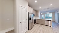 Located at 1951 Integra Dr in West Melbourne, Florida, this well-designed one-bedroom, one-bathroom residence offers a thoughtfully organized single-floor layout that maximizes comfort and functionality. The open-concept kitchen is a standout feature, boasting taupe cabinetry, bright white quartz countertops, a peninsula with an undermount sink, and a full suite of stainless steel appliances including a French door refrigerator, electric range, microwave, and dishwasher. Pendant lighting above the peninsula adds a modern touch, while recessed ceiling lights illuminate the space throughout. Light wood-tone luxury vinyl plank flooring flows seamlessly through the kitchen and living areas, creating a cohesive, airy feel. The living room is bathed in natural light from large windows and a glass door that opens to an outdoor balcony, complemented by a ceiling fan overhead. The bedroom features plush carpet, a ceiling fan, and a generously sized window. The dedicated closet provides convenient storage. The bathroom is finished with a single-sink vanity, quartz countertop, taupe cabinetry, large-format tile surrounding the tub/shower combo, and brushed nickel fixtures, delivering a clean and polished aesthetic throughout.