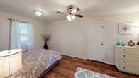 This single-floor home offers a clean, functional layout with warm hardwood flooring that flows seamlessly throughout the living spaces. The kitchen is thoughtfully designed with an abundance of white cabinetry—both upper and lower—providing generous storage, complemented by a double-basin stainless steel sink, a white electric range, and light-toned countertops. A ceiling fan overhead and a window unit ensure comfortable year-round climate control, while a window allows natural light to brighten the space. The bedroom is a comfortable retreat, featuring rich hardwood floors, a ceiling fan with integrated lighting, and soft neutral wall tones that create a calm atmosphere. It conveniently connects to both a walk-in closet and a private ensuite bathroom. The bathroom is distinguished by classic pink tile wainscoting, mosaic tile flooring, a window that invites natural light, a vanity with a framed mirror, and a shower-tub combination. Crown molding details and crisp white trim throughout the home add a polished, cohesive finish. The overall ambiance is bright, tidy, and move-in ready, offering a practical and welcoming living environment.