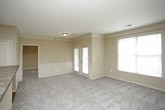 This single-floor residence offers a well-organized layout that balances functional living spaces with comfortable design details throughout. The galley-style kitchen serves as a central hub, featuring warm honey-toned wood cabinetry with raised-panel doors, dark granite-style countertops, and a full suite of black appliances including a refrigerator, electric range, microwave, and dishwasher. Wood-look flooring runs through the kitchen, adding warmth underfoot, while track lighting overhead enhances visibility across the generous counter space and storage.

The living area is carpeted and generously sized, with wainscoting detail along the lower walls, large windows with blinds allowing natural light to fill the room, and a set of French doors providing access to an outdoor space. Additional bedrooms are similarly carpeted, each equipped with ceiling fans and windows overlooking exterior greenery. One bedroom features its own set of French doors leading to a private balcony.

Two bathrooms serve the unit, each finished with wood-look flooring, dark-topped vanities with wood cabinetry, and glass-enclosed tub-shower or shower-only combinations. The neutral warm beige palette used throughout the unit creates a cohesive and inviting atmosphere across all rooms.
