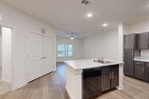 This single-story, one-bedroom, one-bathroom unit offers a thoughtfully designed layout that maximizes its compact footprint. The open-concept living and kitchen area forms the heart of the unit, finished with wood-style plank flooring that extends throughout the main space. The kitchen is well-equipped, featuring dark espresso cabinetry with brushed nickel hardware, granite-look countertops, a peninsula with an integrated sink and dishwasher, and black appliances including a range, microwave, and refrigerator. Recessed lighting and a ceiling fan with a light fixture keep the space bright and comfortable, while a window overlooking the outdoors brings in natural light.

The bedroom is a comfortable size, carpeted for warmth, and includes a ceiling fan and a window. It connects directly to a walk-in closet outfitted with wire shelving, offering generous storage. The full bathroom features a single-vanity with granite-look countertops and dark cabinetry, a tub-shower combination, and wood-style tile flooring. Throughout the unit, the neutral white walls and clean finishes contribute to a bright, modern aesthetic.