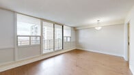 Located at 1150 Fisher Ave in Ottawa's west end, this 2-bedroom, 2-bathroom unit offers a well-designed layout across a single floor. The living room is a standout feature, bathed in natural light through expansive floor-to-ceiling sliding glass doors that open onto a private balcony with open outdoor views — ideal for enjoying Ottawa's skyline. Light hardwood flooring runs throughout the living areas and bedrooms, lending warmth and continuity to the space. A pendant light fixture adds a subtle decorative touch to the living and dining area. The kitchen is thoughtfully appointed with crisp white cabinetry, subway tile backsplash, dark countertops, and neutral tile flooring, connecting seamlessly to the main living area through an open passageway. The generously sized primary bedroom features large windows that frame open views, filling the room with natural light. The second bedroom is well-proportioned with hardwood floors, a closet, and its own window. Two bathrooms serve the unit: one with a white vanity, dark countertop, mirror, and tile flooring, and a second with an extended stone-topped vanity, large mirror, and a tiled shower. The overall palette of warm neutrals and clean finishes creates a bright, calm, and functional living environment.