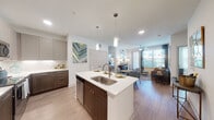 This thoughtfully designed single-floor residence offers a seamless blend of modern aesthetics and functional living. The open-concept layout connects the kitchen, dining, and living areas, creating a bright and inviting atmosphere enhanced by wood-style plank flooring throughout. The kitchen is a standout feature, equipped with stainless steel appliances, two-tone cabinetry in warm walnut and soft gray, crisp white quartz countertops, and a central island with a sink and pendant lighting — ideal for both cooking and casual dining. The living area is generously sized, bathed in natural light from large windows and a sliding glass door, and fitted with a ceiling fan for year-round comfort. The primary bedroom offers ample space, large windows, and direct access to a well-appointed en-suite bathroom featuring a double-sink vanity with dark wood cabinetry, a soaking tub, and clean tile finishes. A second bedroom provides comfortable accommodations with natural light and ceiling fan access to a secondary bathroom with a single vanity. Connecting hallways are finished in light tile, adding to the residence's clean, contemporary feel. The overall ambiance is modern and polished, with consistent finishes and thoughtful design details throughout.