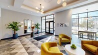This thoughtfully designed amenity floor offers a seamless blend of elegance and functionality across a generous single-level layout. The entrance lobby immediately impresses with its striking geometric marble-look tile flooring, a coffered ceiling adorned with a sculptural sputnik chandelier, and floor-to-ceiling glass doors that flood the space with natural light and urban views. Plush gold velvet armchairs and a console table with curated decor create an inviting lounge atmosphere, while a wet bar with teal cabinetry and dark countertops adds a refined, hospitality-inspired touch.

The hallway extends from the lobby with a clean, modern aesthetic, featuring patterned carpeting, dark-framed numbered doors with gold accents, and warm wall sconces. A dedicated mailroom area is anchored by a rich wood accent wall housing resident mailboxes, lit by globe pendant chandeliers overhead.

The fitness center is a standout space, boasting warm hardwood floors, floor-to-ceiling windows offering sweeping outdoor views, bold decorative wallpaper, wall-to-wall mirrors, and modern pendant lighting. Cardio equipment is well-positioned to take advantage of the natural light. Restroom facilities are also accessible from the lobby corridor, finished with dark panel doors and elegant signage, completing this polished and well-appointed amenity level.