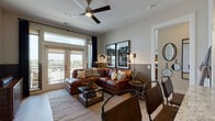 This single-floor residence offers a thoughtfully designed layout that balances style and functionality. The living room serves as the centerpiece of the space, featuring warm hardwood-style flooring, a ceiling fan, and floor-to-ceiling French doors that open to a private balcony with open outdoor views. Natural light pours in through large windows framed by dark curtains, creating a bright yet cozy atmosphere complemented by rich cognac leather sectional seating and contemporary wall art.

The kitchen is equipped with dark espresso cabinetry, stainless steel appliances including a gas range, microwave, and French door refrigerator, topped with striking granite countertops and a tile backsplash. A generous island provides additional prep and seating space.

Both bedrooms feature plush carpeting, large windows with outdoor views, and warm, modern décor. The primary bedroom includes a leather-upholstered headboard and ample natural light, while the second bedroom offers a similarly inviting atmosphere with artistic wall accents.

The bathrooms are finished with large-format tile flooring, dark wood vanity cabinetry, granite countertops, and oversized mirrors. The full bathroom includes a tub-shower combination with tiled surround. Throughout, the design maintains a cohesive, contemporary aesthetic with warm tones and quality finishes.