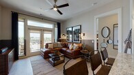 This single-floor residence offers a thoughtfully designed layout that balances style and functionality. The living room serves as the centerpiece of the space, featuring warm hardwood-style flooring, a ceiling fan, and floor-to-ceiling French doors that open to a private balcony with open outdoor views. Natural light pours in through large windows framed by dark curtains, creating a bright yet cozy atmosphere complemented by rich cognac leather sectional seating and contemporary wall art.

The kitchen is equipped with dark espresso cabinetry, stainless steel appliances including a gas range, microwave, and French door refrigerator, topped with striking granite countertops and a tile backsplash. A generous island provides additional prep and seating space.

Both bedrooms feature plush carpeting, large windows with outdoor views, and warm, modern décor. The primary bedroom includes a leather-upholstered headboard and ample natural light, while the second bedroom offers a similarly inviting atmosphere with artistic wall accents.

The bathrooms are finished with large-format tile flooring, dark wood vanity cabinetry, granite countertops, and oversized mirrors. The full bathroom includes a tub-shower combination with tiled surround. Throughout, the design maintains a cohesive, contemporary aesthetic with warm tones and quality finishes.