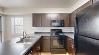 Located at 1175 Albion St in Denver's Hale neighborhood, this single-floor unit offers a practical and well-appointed layout that makes efficient use of its compact footprint. The combined kitchen and living area forms the heart of the space, where function meets everyday comfort.

The kitchen is outfitted with rich, dark-stained cabinetry featuring sleek hardware, dark granite-style countertops, and a peninsula with a double stainless steel sink — ideal for both meal prep and casual dining. Black appliances, including a range, over-the-range microwave, and refrigerator, complement the cabinetry's bold tones. Light hardwood-style flooring runs throughout, adding warmth and continuity across the space.

The living area is bright and open, bathed in natural light from a large sliding glass door that leads to a private balcony with views of mature trees. A tiled fireplace anchors the room, providing a cozy focal point, while baseboard heating runs along the walls for year-round comfort. A textured ceiling adds a classic residential touch throughout.

A connecting hallway links the living area to additional rooms, with crisp white walls and clean finishes maintaining a neutral, versatile aesthetic. The overall ambiance is functional, comfortable, and well-suited to everyday urban living in Denver.