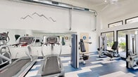 Located at 2380 Sierra Blvd in Sacramento, CA, this fitness center offers a thoughtfully designed exercise space that balances functionality with modern aesthetics. The room features soaring vaulted ceilings that create an open, airy atmosphere, complemented by exposed metallic ductwork that adds an industrial design element. Ceiling fans and recessed lighting ensure the space remains comfortable and well-lit throughout the day.

Large glass double doors and expansive windows on multiple walls flood the interior with abundant natural light while offering views of the surrounding greenery, creating an inviting environment for workouts. The eye-catching blue, white, and gray geometric patterned flooring adds a dynamic visual energy to the space.

The fitness center is well-stocked with a variety of cardio equipment, including treadmills and stationary bikes, as well as multiple strength training machines to support a comprehensive workout routine. Full-length mirrors along one wall visually expand the space and assist users during exercise. A decorative mountain range wall graphic adds a sporty, motivational touch to the clean white walls. Accessible restroom facilities are also available within the space, ensuring convenience for all users.