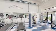 Located at 2380 Sierra Blvd in Sacramento, CA, this fitness center offers a thoughtfully designed exercise space that balances functionality with modern aesthetics. The room features soaring vaulted ceilings that create an open, airy atmosphere, complemented by exposed metallic ductwork that adds an industrial design element. Ceiling fans and recessed lighting ensure the space remains comfortable and well-lit throughout the day.

Large glass double doors and expansive windows on multiple walls flood the interior with abundant natural light while offering views of the surrounding greenery, creating an inviting environment for workouts. The eye-catching blue, white, and gray geometric patterned flooring adds a dynamic visual energy to the space.

The fitness center is well-stocked with a variety of cardio equipment, including treadmills and stationary bikes, as well as multiple strength training machines to support a comprehensive workout routine. Full-length mirrors along one wall visually expand the space and assist users during exercise. A decorative mountain range wall graphic adds a sporty, motivational touch to the clean white walls. Accessible restroom facilities are also available within the space, ensuring convenience for all users.