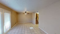 This two-story townhouse offers four bedrooms and two and a half bathrooms across a well-organized layout designed for comfortable everyday living. The main level features light-toned ceramic tile flooring throughout the living and dining areas, both equipped with ceiling fans. A set of French doors in the dining area provides access to the outdoors, allowing natural light to flow into the space. The galley-style kitchen is outfitted with warm wood cabinetry, light countertops, a stainless steel refrigerator, a gas range, and a double basin sink, with a pass-through opening to adjacent living areas. A staircase with carpeted treads connects the main level to the upper floor. The bedrooms upstairs are carpeted and include ceiling fans, with windows fitted with blinds that bring in natural light. Two full bathrooms feature tub-shower combinations with tile surrounds, single-sink vanities with wood cabinetry, and tile flooring. A half bathroom is also present on the main level. Textured ceilings and neutral wall tones are consistent throughout, giving the townhouse a cohesive, understated aesthetic.