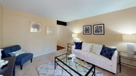This single-floor residence offers a thoughtfully designed layout with distinct living, dining, kitchen, bedroom, and bathroom areas, all unified by a warm neutral color palette accented with blue and gold tones. The living room features plush carpeting, smooth walls painted in a soft beige, and a sliding glass door that allows natural light to fill the space while providing access to an outdoor area. A glass-top coffee table and contemporary furnishings contribute to the room's open, airy feel.

Adjacent to the living room, the dining area accommodates a round glass table beneath a multi-light chandelier, with a large window fitted with horizontal blinds enhancing the brightness of the space. The kitchen is equipped with rich wood cabinetry, dark granite-style countertops, a double stainless steel sink, and black appliances, all set over durable wood-look flooring.

The bedroom is generously sized with soft carpeting, a ceiling fan, and a window with sheer curtains that invite natural light. A seating area adds versatility to the room. The bathroom features a wide vanity with dark countertops, wood-toned cabinetry, a large mirror, and wood-look flooring, completing the residence's cohesive and practical design.