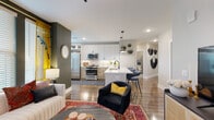 This single-floor residence makes a striking first impression with its bold, eclectic interior design and thoughtful layout. A welcoming hallway, adorned with dramatic sculptural wall art, leads into the open-concept main living area where hardwood flooring flows seamlessly throughout. The living room features deep olive-green accent walls, large windows dressed with golden-yellow curtains, and abundant natural light. A curved channeled sofa, layered rugs, and a sculptural chandelier contribute to the space's artistic character.

The kitchen is well-appointed with stainless steel appliances including a gas range, built-in microwave, and dishwasher. White upper cabinetry contrasts with warm wood-toned lower cabinets, complemented by a white quartz island with a built-in wine cooler and pendant lighting above. A textured tile backsplash adds visual depth.

The primary bedroom features a charcoal accent wall, carpet flooring, and an en-suite bathroom with a dual-sink wood-toned vanity, herringbone tile walls, and built-in shelving. A spacious walk-in closet with wire shelving provides generous storage. The secondary bedroom offers a vibrant burnt-orange accent wall and natural light, served by a second full bathroom with large-format tile flooring and a tub-shower combination.