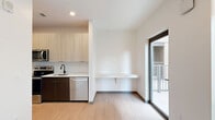 Located at 421 N Pennsylvania St in downtown Indianapolis, this thoughtfully designed studio offers a clean, contemporary aesthetic across a single floor. Light wood-tone flooring runs throughout the unit, complementing the bright white walls and creating a cohesive, modern feel.

The open-concept kitchen and living area serves as the heart of the space. The kitchen is appointed with light wood upper cabinetry, contrasting dark lower cabinets, white subway tile backsplash, stainless steel appliances including a range, microwave, and dishwasher, and a black matte sink fixture. A built-in wall-mounted shelf provides a functional workspace or dining surface, while large sliding glass doors flood the living area with natural light and open to a private balcony with views of the surrounding cityscape.

The bathroom features warm wood cabinetry with a white vanity countertop, a glass-enclosed shower, and light flooring that continues the unit's cohesive palette. A dedicated laundry area houses a stacked washer and dryer unit for added convenience. The space also includes a closet and a utility room, maximizing storage and functionality. Recessed lighting throughout ensures a well-lit, polished environment.