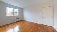 Located at 1130 Falls Hill Drive in Baltimore's 21211 zip code, this single-floor unit offers a straightforward and functional layout with consistent design elements throughout. Rich, warm-toned hardwood flooring runs through the main living areas and bedrooms, adding character and a sense of continuity across the space.

The living area is open and well-lit, with a large window that allows natural light to fill the room and frames views of the surrounding neighborhood. A radiator unit beneath the window provides efficient heating, and neutral light gray walls create a clean, versatile backdrop. The entry door is conveniently situated within the living space.

The bedroom mirrors the living area in its simplicity, featuring the same hardwood floors, neutral walls, and a window with neighborhood views. A baseboard radiator ensures year-round comfort.

The kitchen is thoughtfully appointed with rich dark espresso cabinetry, light marbled countertops, a stainless steel single-basin sink, and a gas range with overhead ventilation. A stainless steel refrigerator completes the appliance suite, offering a cohesive and practical cooking space.

The bathroom is bright and clean, featuring a full soaking tub with shower, a toilet, and a dark-cabinetry vanity with a white countertop that echoes the kitchen's design aesthetic. A window provides natural ventilation and light, enhancing the overall freshness of the space.