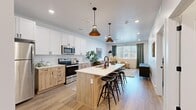 Located along W River View Way in Provo, Utah, this thoughtfully designed one-bedroom, one-bathroom residence offers a clean, modern aesthetic throughout. The open-concept layout seamlessly connects the kitchen and living room, creating an inviting and functional shared space. The kitchen is a standout feature, showcasing a two-tone cabinetry design with crisp white upper cabinets and warm natural wood lower cabinets, complemented by a herringbone tile backsplash and stainless steel appliances. A central island with a white countertop and bar seating serves as a natural gathering point, illuminated by stylish pendant lights overhead. Light wood-style flooring extends throughout the main living areas, enhancing the bright and airy feel. The living room benefits from large windows that invite natural light and offer views of the surroundings. The bedroom is a serene retreat featuring plush carpet, a generous window with ample natural light, and direct access to a well-sized walk-in closet complete with built-in shelving and in-unit laundry. The bathroom mirrors the home's modern design with warm wood cabinetry, a white countertop vanity, and black hardware accents. This unit offers a cohesive, contemporary living experience in a desirable Provo location.