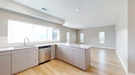 Located along State Line Road in Kansas City, KS, this well-appointed 2-bedroom, 2-bathroom residence offers a thoughtfully designed single-floor layout with a clean, contemporary aesthetic throughout. The open-concept kitchen and living area serves as the heart of the home, featuring light wood flooring, recessed lighting, and an abundance of natural light streaming through large windows with city views. The kitchen is outfitted with stainless steel appliances including a dishwasher, microwave, and range, complemented by crisp white upper cabinetry, grey lower cabinetry, a white quartz peninsula, and a classic tile backsplash. A bright hallway connects the main living area to the private quarters. The primary bedroom is a comfortable retreat with plush carpeting, multiple windows framing urban views, a sliding glass door opening to a private balcony, and a dedicated walk-in closet with wire shelving. The primary bathroom features a double-sink vanity with blue-grey cabinetry, a glass-enclosed shower, and light wood flooring. The second bedroom also offers carpeted floors and natural light. The second bathroom includes a full tub-shower combination, a single-sink vanity with dark cabinetry, and wood flooring. Two closets provide ample storage throughout the residence.