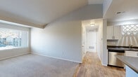This single-floor residence offers a thoughtfully designed layout that balances comfort and functionality throughout. The living room serves as the heart of the home, featuring vaulted ceilings that create a sense of openness and volume, plush neutral carpeting underfoot, and a tile-surround fireplace with a clean white mantel as a standout focal point. A large window floods the space with natural light while offering views of the surrounding neighborhood. The flooring transitions seamlessly from carpet in the living area to warm wood-tone hardwood in the hallway and kitchen, providing a cohesive aesthetic flow. The kitchen is well-equipped with ample white shaker-style cabinetry, dark countertops, stainless steel appliances including a range, over-the-range microwave, and a side-by-side refrigerator with ice and water dispenser. A center island with additional counter space adds both workspace and versatility. The bathroom features a white vanity with dark countertops, a large mirror, and a bright window that brings in natural light. The bedrooms are carpeted and generously sized, with multiple windows providing natural light and neighborhood views. One bedroom includes a dedicated closet with built-in shelving. Clean neutral tones and white trim are consistent throughout, lending the space a bright and move-in ready character.