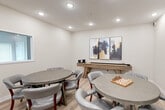 Located at 42280 Garfield Rd in Clinton Township, Michigan, this single-floor amenity space offers a thoughtfully designed environment for recreation and socializing. The layout spans a generous footprint and is organized around a central, extended hallway that sets a polished tone from the moment of arrival. The corridor is finished with a sophisticated combination of textured dark accent walls, crisp white wainscoting, and patterned carpeting underfoot. Recessed and flush ceiling lighting illuminates the space evenly, while a stylish seating vignette near the elevator landing adds a welcoming touch.

The game room is a bright, open gathering space featuring light wood-look flooring, recessed lighting, and round game tables with upholstered rolling chairs — ideal for card games and chess. A shuffleboard table anchors one wall, accompanied by abstract wall art that adds a contemporary flair. An adjacent nook includes a wall-mounted television and a rustic sideboard stocked with board games, creating a cozy entertainment corner.

A dedicated screening lounge offers rows of plush, tan leather armchairs arranged theater-style, complete with a classic red popcorn machine and a large projection wall. Additional rooms provide bright, windowed spaces with natural light, casual seating, and a dining area with a sleek table and light blue chairs — rounding out this well-appointed amenity level.