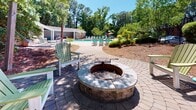 Located at 1551 Sam Rittenberg Blvd in Charleston, SC, this thoughtfully designed outdoor amenity space offers residents a rich array of leisure features set within a beautifully landscaped environment. At the heart of the space is a generous resort-style swimming pool, surrounded by teal Adirondack lounge chairs and framed by mature trees that provide natural shade and privacy. A colorful umbrella adds a vibrant touch to the poolside atmosphere.

A standout feature is the circular stone fire pit, centrally positioned on a paver patio and accompanied by Adirondack chairs arranged to encourage conversation and relaxation. The paver pathway connects the fire pit area to the pool, creating a cohesive outdoor flow. For those seeking a quieter retreat, a hammock is strung between tall pines along the perimeter, nestled under a canopy of mature trees with dappled sunlight filtering through.

Dense, well-maintained shrubbery and flowering plants define the borders of the space, enhancing both privacy and visual appeal. Mulched garden beds and pine straw ground cover contribute to the natural, low-maintenance aesthetic. The overall ambiance is serene and inviting, blending Southern charm with resort-inspired amenities — ideal for unwinding, socializing, or simply enjoying the outdoors in the heart of Charleston.