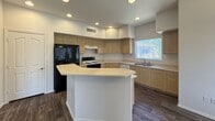 Located at 13621 W Glendale Ave, Unit 110 in Glendale, AZ, this single-story residence offers 1,340 square feet of well-organized living space across three bedrooms and two bathrooms. Dark hardwood-style flooring runs consistently throughout the home, providing a cohesive and clean aesthetic.

The open living area greets you at the entry, featuring large windows with vertical blinds that allow ample natural light. The kitchen is a functional highlight, equipped with light wood cabinetry, light-toned countertops, a black refrigerator, an electric range, and a built-in sink. A peninsula with a curved countertop adds prep space and separates the kitchen from the living area. Recessed lighting illuminates the space effectively.

The primary bedroom measures a spacious 260 square feet and includes a ceiling fan, while additional bedrooms offer comparable comfort and access to closet space. Both bathrooms feature tub-shower combinations enclosed by sliding glass doors and distinctive glass block windows that provide natural light while maintaining privacy.

A dedicated laundry room houses a full-size washer and dryer with overhead shelving for added storage. The hallway connects all rooms efficiently, completing this practical and move-in ready floor plan.