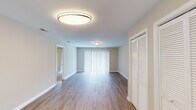 This single-floor residence offers a thoughtfully designed layout that balances open living spaces with comfortable private quarters. The expansive main living area is finished with durable wood-style flooring and neutral warm-toned walls, creating a bright and welcoming atmosphere. Vertical blinds cover a large sliding glass door that fills the room with natural light, while a louvered closet provides convenient storage near the entryway. The kitchen is outfitted with crisp white shaker-style cabinetry, white countertops, a double stainless steel sink, and black appliances including a refrigerator, range, and dishwasher. Track lighting illuminates the workspace, and a window above the sink brings in additional natural light. The bedrooms feature plush carpeting and are generously sized, each benefiting from windows with outdoor views of greenery. One bedroom includes a sliding glass door providing direct outdoor access. The primary bathroom features a full tub and shower combination, while a second bathroom offers a white vanity with an integrated sink and a well-lit mirror. Throughout the residence, clean white trim, neutral tones, and consistent finishes contribute to a cohesive and move-in-ready aesthetic.
