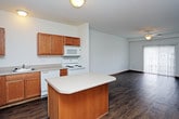 This single-floor residence offers a well-organized, open layout with consistent hardwood-style flooring flowing seamlessly throughout every room. The kitchen is a functional highlight, featuring warm oak cabinetry both above and below the countertops, a central island that provides additional prep and storage space, a stainless steel sink, and white appliances including a refrigerator, electric range, microwave, and dishwasher. The kitchen opens directly into the living area, creating a connected and sociable atmosphere ideal for everyday living.

The spacious living room is bathed in natural light through a large sliding glass door that leads to an outdoor area, and is equipped with a ceiling fan for year-round comfort. Additional rooms include a bright bedroom with a generously sized window offering pleasant outdoor views and its own ceiling fan, as well as a utility room with electrical panel access that connects back to the kitchen. The bathroom is well-appointed with warm wood cabinetry, a light countertop vanity, and ample towel bar storage. Multiple closets with bifold doors provide generous storage throughout the unit. The clean white walls and warm wood tones throughout lend the space a bright, welcoming ambiance.