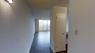 This single-floor space is characterized by its clean, minimalist design and functional layout. The interior showcases rich, dark hardwood flooring that runs throughout, providing a striking contrast against the crisp white walls and trim. A hallway leads into an open living area, where a large sliding glass door floods the space with natural light and provides direct access to an outdoor balcony, offering views of the surrounding exterior. The white walls are smooth and well-maintained, contributing to the bright and open ambiance of the space. A full-height interior door with a classic round knob is positioned along the hallway, providing access to an additional room or closet. The layout flows naturally from the entry corridor into the main living area, creating a sense of depth and openness. The combination of dark flooring, white walls, and abundant natural light from the floor-to-ceiling sliding door gives the space a modern yet neutral aesthetic, making it highly versatile. The balcony access further enhances the livability of the space, blending indoor and outdoor living seamlessly. Overall, the space presents a clean, move-in ready environment with a straightforward and practical design.