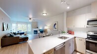 Located at 25800 SW Canyon Creek Rd in Wilsonville, Oregon, this well-appointed 2-bedroom, 3-bathroom single-floor residence offers a thoughtfully designed open-concept layout with light wood-tone flooring throughout the main living areas. The combined living and dining area is anchored by a corner gas fireplace and ceiling fan, with large windows framing views of the surrounding natural landscape and filling the space with abundant natural light. A picture rail along one wall adds a curated, gallery-like touch to the living room. The kitchen features a peninsula with a white quartz countertop, stainless steel appliances including a refrigerator and microwave, light wood cabinetry, track lighting, and a stainless steel sink — all open to the dining and living areas for seamless entertaining. Built-in shelving provides additional storage and display space. The primary bedroom is a comfortable retreat with sliding glass door access to a private balcony overlooking greenery, plush carpeting, and a ceiling fan. The second bedroom features large windows with outdoor views and soft carpeting. The bathrooms are clean and bright, with light wood vanities, white countertops, and a tub-shower combination. Two closets and thoughtfully placed storage throughout complete this functional and inviting home.