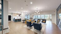 Located at 450 Warrenville Rd in Lisle, IL, this generously sized single-floor amenity space offers a thoughtfully designed environment built for comfort, community, and productivity. The welcoming entry features large-format tile flooring, clean white walls, and a built-in service counter accented by natural stone tile, setting a polished tone from the moment of arrival. A curved hallway adorned with a striking wood sculptural art installation guides visitors deeper into the space. The expansive open lounge area serves as the heart of the floor, combining warm hardwood-style flooring with a sophisticated mix of seating arrangements — from mustard yellow sofas and navy accent chairs to mid-century-inspired armchairs — all illuminated by decorative globe and multi-arm chandeliers. Floor-to-ceiling windows flood the area with natural light and offer lush outdoor views. A kitchen-style bar with teal cabinetry, quartz countertops, and pendant lighting provides a social gathering spot alongside communal dining and high-top seating. A dedicated lounge nook features a teal geometric accent wall and mounted TV. The well-equipped fitness center, visible in the floorplan, offers a comprehensive range of exercise equipment. Private meeting rooms with carpeted floors, track lighting, and curated artwork complete the offering, making this a versatile and refined amenity destination.