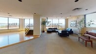 Located at 1301 S Second Ave in Minneapolis, this single-floor space offers a thoughtfully designed layout suited for gatherings and entertaining. The interior is defined by its white-painted brick walls, carpeted floors, and recessed and track lighting throughout, creating a warm yet polished atmosphere.

A central highlight is the skylit atrium corridor, where a glazed ceiling floods the space with natural light, casting geometric shadow patterns across the carpet and illuminating the white brick architecture. This passageway connects the various zones of the space seamlessly.

The main lounge area features floor-to-ceiling windows that frame sweeping elevated views of the Minneapolis skyline and surrounding landscape. A sectional seating arrangement anchors this room, complemented by large-scale artwork displayed on the walls. A grand piano and additional seating create a dedicated music and relaxation corner nearby.

A full bar area is equipped with a granite-topped counter, built-in bar stools, track lighting, and a backlit liquor display, making it well-suited for hosting events. A staircase with ornamental iron railings connects to an adjacent level, adding architectural character.

Throughout the space, the combination of natural light, elevated views, curated artwork, and versatile room configurations contributes to an inviting and multifunctional environment.
