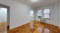 This single-floor unit offers a thoughtfully laid-out interior defined by its classic parquet hardwood flooring, which runs throughout the living spaces and adds warmth and character to every room. The living area is bright and open, with white walls and multiple windows fitted with blinds, allowing natural light to fill the space. A radiator provides heating, and a wall-mounted air conditioning unit ensures year-round comfort. An elegant arched doorway connects the main living area to an adjoining room, enhancing the sense of flow between spaces.

The kitchen is a standout feature, showcasing dark espresso cabinetry paired with sleek granite countertops in a classic salt-and-pepper pattern. A stainless steel undermount sink completes the look, giving the kitchen a modern, polished feel that contrasts beautifully with the unit's traditional parquet floors.

The bathroom is clean and functional, finished entirely in white tile. It features a full-size soaking tub with an overhead shower, a pedestal sink, and a frosted window that brings in natural light while maintaining privacy. The all-white palette gives the bathroom a crisp, timeless appearance. Overall, this space blends classic architectural details with updated finishes for a comfortable and functional living environment.