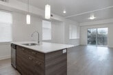 This contemporary single-floor residence offers a thoughtfully designed open-concept layout that seamlessly connects the kitchen and living areas. The kitchen serves as a central hub, anchored by a sleek island with a double stainless steel sink, white quartz countertops, and warm wood-toned cabinetry. Stylish pendant lighting hangs above the island, complementing the light hardwood flooring that flows throughout the main living spaces. The living area opens directly onto a private balcony through sliding glass doors, offering serene views of a natural hillside landscape.

The two bedrooms are carpeted for comfort and each features windows with the same picturesque outdoor views, filling the rooms with natural light. A spacious walk-in closet with built-in shelving and hanging rods provides generous storage. Both bathrooms are finished with light tile flooring, white subway-tiled tub-shower combinations, wood-accented vanities, and white quartz countertops, maintaining a clean and consistent aesthetic throughout.

A dedicated in-unit laundry room equipped with a full-sized washer and dryer adds everyday convenience. The space as a whole presents a clean, modern design with a neutral palette, making it a bright and functional home.