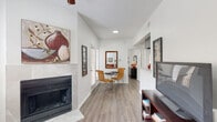 This single-floor residence offers a thoughtfully designed layout that balances comfort and functionality. The living area serves as the heart of the home, featuring wood-look flooring, a ceiling fan, a textured ceiling, and a tile-surround fireplace that anchors the room. Natural light filters in through slatted window blinds, and the open flow connects the living space to a compact dining nook with a glass-top table, creating a seamless entertaining area. A dedicated media zone with a TV console completes the living room arrangement.

The galley-style kitchen is efficiently organized with gray cabinetry, speckled countertops, and stainless steel appliances including a refrigerator, range, and dishwasher. Adjacent utility access adds everyday convenience.

The unit includes two bedrooms, each with wood-look flooring and window blinds. The primary bedroom features a textured ceiling and is complemented by a walk-in closet with built-in shelving and hanging rods. The bathroom corridor leads to a tiled tub-shower combination with a large mirror and access to additional closet space.

Throughout the home, crisp white walls, consistent flooring, and clean lines create a bright, cohesive ambiance that is both practical and inviting.