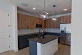 This well-designed 560-square-foot, one-bedroom, one-bathroom apartment at 2380 Staples Rd in San Marcos, Texas offers a modern living experience with thoughtfully selected finishes throughout. Light wood-look flooring runs seamlessly across the entire single-floor layout, creating a cohesive and clean aesthetic.

The kitchen is a standout feature, showcasing a two-tone cabinet design with warm wood-grain upper cabinets and slate-blue lower cabinets, all accented by matte black hardware. Dark granite countertops extend to a central island equipped with an undermount sink and a matte black pull-down faucet. Stainless steel appliances, including a French door refrigerator, electric range, and over-the-range microwave, are complemented by a white subway tile backsplash. Globe pendant lights above the island add a contemporary touch.

The 130-square-foot primary bedroom features crisp white walls, clean baseboard trim, and a window with blinds that allows natural light and neighborhood views. A dedicated closet provides practical storage.

The bathroom is efficiently appointed with dark cabinetry, a combined tub and shower with tile surround and a built-in niche, and matte black fixtures consistent with the unit's modern design language. White panel doors with matte black hardware are found throughout, tying the aesthetic together cohesively.