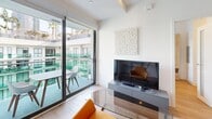This contemporary 660 square foot apartment, located in a downtown high-rise at #923TENTEN, showcases efficient design and modern aesthetics. The single-floor layout comprises one bedroom (160 sq ft), one bathroom, a kitchen, and a living room. The kitchen features sleek cabinetry combining light wood upper cabinets with darker lower units, stainless steel appliances, and a striking white backsplash. Recessed lighting and under-cabinet illumination enhance the space's brightness. The bathroom boasts a modern vanity, large mirror with LED lighting, and a glass-enclosed shower. Throughout the apartment, warm wood flooring creates a cohesive look. The bedroom, while compact, includes built-in storage solutions. Large windows in the living area and bedroom offer impressive city views, flooding the space with natural light and showcasing the surrounding urban landscape. The building itself features a multi-story design with glass balconies, providing residents with outdoor spaces. This apartment combines urban sophistication with practical living in the heart of the city.