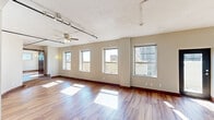 Located in the heart of downtown Dallas at 1501 Main St, this loft-style unit offers a distinctive urban living experience defined by open layouts, rich hardwood flooring, and generous natural light throughout. The elongated floor plan encompasses three living areas, each bathed in sunlight streaming through large windows that frame views of the surrounding Dallas cityscape. Ceiling fans are featured throughout, adding both function and character.

The kitchen is sleek and well-appointed, featuring dark cabinetry, white tile backsplash, stainless steel appliances including a refrigerator, microwave, and range, along with pendant and track lighting that illuminate the space stylishly. An adjacent glass door leads to additional outdoor access, enhancing the flow of the unit.

Two bathrooms serve the space, one offering a glass-enclosed walk-in shower with subway tile surround and brushed nickel fixtures, and another featuring wood-toned cabinetry, a white countertop vanity with mirror, and hardwood flooring. Exposed ductwork in the bathrooms adds to the loft aesthetic.

A dedicated laundry room provides full-size washer and dryer units alongside built-in wire shelving for storage. A closet with sliding mirrored doors offers additional organization. Track lighting and ceiling fans throughout complete this well-designed urban retreat.