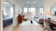 Located at 34 Munroe St in Lynn, MA, this thoughtfully designed single-floor residence offers a seamless blend of modern finishes and functional living. The open-concept layout connects the kitchen and living area, creating a bright, cohesive space bathed in natural light from large windows that frame views of the surrounding neighborhood streetscape.

The kitchen is outfitted with light gray shaker-style cabinetry, stainless steel appliances including a range, microwave, and refrigerator, and a dark subway tile backsplash that provides a striking contrast. A built-in breakfast bar with seating offers a practical dining solution, while light hardwood flooring ties the entire space together.

The living area provides a comfortable retreat with recessed lighting and generous window views, creating an airy and welcoming atmosphere. The bedroom is a calm, well-proportioned space featuring the same warm hardwood flooring and ample room for furnishings.

The full bathroom is finished with large-format subway tile surrounding the tub-shower combination, a floating vanity with LED-backlit mirrors, and sleek matte black fixtures. A stacked washer and dryer unit is conveniently integrated into the bathroom, adding practical in-unit laundry access. Throughout the residence, clean lines, neutral tones, and quality materials establish a polished, contemporary aesthetic.
