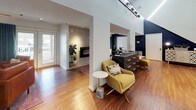 The Abbington Hills Clubhouse is a thoughtfully designed single-floor community space that blends modern aesthetics with welcoming functionality. The interior is immediately distinguished by its dramatically high ceilings, which lend an open, airy quality to the main area. Warm wood-look flooring flows throughout, providing a cohesive foundation that complements the bold design choices found across the space.

A striking navy blue accent wall serves as a unifying architectural element, appearing in multiple areas and creating visual depth against the crisp white walls. The reception and common area features a dark counter-height bar with woven accent stools, a beverage station, and vibrant abstract artwork arranged in a grid above — adding a lively burst of color.

A dedicated lounge area offers comfortable leather seating, colorful rugs, and a wall-mounted television, with direct access to an outdoor space through glass doors that invite natural light. An adjacent room features a sleek linear fireplace set into a tile surround, accompanied by lush greenery for a relaxed atmosphere.

A decorative credenza beneath a dramatic angled navy wall adds an artful focal point, while the overall layout supports both casual gatherings and community activities with ease.
