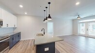 Located at 347 Arboretum Dr in Wilmington, NC, this single-floor residence offers a thoughtfully designed open-concept layout with contemporary finishes throughout. The kitchen serves as the centerpiece of the home, showcasing a bold two-tone design with navy lower cabinets, crisp white upper cabinetry, and a striking speckled granite island topped with a matte black sink and faucet. A decorative geometric tile backsplash complements stainless steel appliances, including a range, microwave, and refrigerator. Three industrial-style pendant lights hang above the island, adding a modern touch. Light wood-look flooring flows seamlessly throughout the entire space, connecting each area cohesively. The living area is bright and open, featuring French doors that invite natural light and provide outdoor access, complemented by a ceiling fan overhead. Bedrooms are well-proportioned, each with large windows offering neighborhood views and ceiling fans for comfort. The bathrooms are finished with white subway tile surrounds, granite-topped white vanities, and matte black hardware and fixtures for a clean, contemporary aesthetic. A stacked in-unit washer and dryer is conveniently accessible from the primary bathroom area, adding practical functionality to this well-appointed home.
