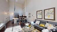 This two-story residence is defined by its dramatic double-height ceilings in the main living area, creating an expansive, loft-inspired atmosphere. Floor-to-ceiling windows on the upper level flood the space with natural light and offer outdoor views, further enhancing the sense of openness throughout.

The main floor features an open-concept layout connecting the living, dining, and kitchen areas. The kitchen is outfitted with stainless steel appliances, a gas range, a striking hexagonal tile backsplash, quartz countertops, and two-tone cabinetry in light and warm wood tones. A half bathroom on the main level adds convenient functionality.

The upper level houses the primary bedroom, which features exposed ductwork lending an industrial character, along with a ceiling fan, carpet flooring, a walk-in closet, and direct access to a private balcony. The full bathroom on this level includes a wood-toned vanity, stone countertop, a soaking tub, and large-format tile flooring. An additional bedroom with a sliding barn-style door, ceiling fan, and walk-in closet is also found on the upper floor, served by a full bathroom with similar refined finishes throughout.