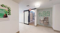 Located at 3 Executive Drive in Evesham, NJ, this thoughtfully designed single-floor fitness and wellness facility offers a well-appointed layout across a generously sized footprint. The space is defined by clean, contemporary architecture, tray ceilings with warm accent lighting, and a cohesive neutral palette throughout.

The centerpiece is a spacious, fully equipped exercise room featuring floor-to-ceiling windows that flood the space with natural light and provide sweeping views of the surrounding wooded landscape. The fitness area includes cardio machines, free weights, a dumbbell rack, treadmills, cable equipment, and a punching bag, all set on durable rubberized flooring. Large mirrors amplify the sense of space and functionality.

A separate lounge or relaxation room features light hardwood flooring, a coffered ceiling with ambient uplighting, a large-scale wall mural, and floor-to-ceiling glass doors opening to an outdoor patio area — creating a calm, restorative environment.

The hallways connecting the spaces are clean and welcoming, featuring large-format tile flooring, globe pendant lighting, a water station set against a decorative mosaic tile accent wall, and curated artwork. Built-in open shelving with integrated lighting and a sculptural console table add refined, functional detail throughout the transitional areas, completing a polished and inviting wellness environment.