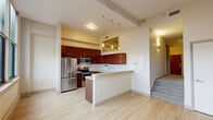 Located at 1201 E. Market St in Akron, Ohio, this one-bedroom, one-bathroom unit offers a thoughtfully organized layout across a single floor. The open-concept kitchen and dining area serves as the heart of the home, showcasing rich dark wood cabinetry, a white subway tile backsplash, stainless steel appliances including a refrigerator, range, and microwave, and a breakfast bar with pendant lighting overhead. Light hardwood-style flooring extends throughout this main living area, creating a bright and welcoming atmosphere. A dedicated entrance leads into the space, with a staircase rising to the private bedroom level. The bedroom is a comfortable retreat finished with plush carpeting, a ceiling fan, a double-door closet, and a window that invites natural light. An additional closet provides further storage convenience. The full bathroom features a tub-shower combination, white tile flooring, and a dark wood vanity that coordinates with the kitchen's cabinetry. A dedicated laundry area adds everyday practicality. A carpeted hallway connects the rooms, completing this efficient and well-appointed residential unit in the heart of Akron.