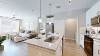 This thoughtfully designed 2-bedroom, 2-bathroom residence spans a single floor and offers a cohesive open-concept layout that maximizes functionality and comfort. The kitchen serves as a central hub of the home, featuring white shaker cabinetry, granite countertops, a subway tile backsplash, stainless steel appliances, and a large island with bar seating illuminated by stylish pendant lights. Light wood-style flooring flows throughout the main living areas, enhancing the bright, airy ambiance. The living room is generously proportioned, filled with natural light from large windows, and finished with a ceiling fan for year-round comfort. The primary bedroom offers a comfortable retreat with plush carpeting, a ceiling fan, and a well-sized window that brings in natural light. Its ensuite bathroom includes granite vanity countertops, white cabinetry, wood-look tile flooring, and direct access to a dedicated walk-in closet. The second bedroom also features carpet flooring and ample natural light. Both bathrooms maintain consistent, modern finishes throughout. A dedicated in-unit laundry room with side-by-side washer and dryer adds everyday convenience. Neutral tones and clean architectural lines give the entire residence a polished, contemporary character.