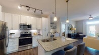 Located at 900 Doverside Dr in Apex, NC, this thoughtfully designed single-floor residence offers a seamless blend of modern finishes and functional living spaces. The open-concept kitchen serves as the heart of the home, featuring white shaker cabinetry reaching toward the ceiling, stainless steel appliances, subway tile backsplash, and a granite-topped island with a double undermount sink and pendant lighting — ideal for both everyday meals and entertaining. Rich hardwood-style flooring flows throughout the main living areas, adding warmth and continuity.

The living room is bright and inviting, highlighted by a ceiling fan, large French doors that open to a private balcony, and generous natural light. The primary bedroom offers a comfortable, carpeted retreat with soft neutral tones and ample natural light, complemented by a spacious walk-in closet outfitted with multi-tiered wire shelving. The second bedroom also features plush carpeting and a calm, well-lit atmosphere. The bathroom includes a granite-topped vanity with white cabinetry and tile flooring, maintaining the home's consistent, refined aesthetic. A dedicated laundry room with a full-size washer and dryer and a stylish barn door accent rounds out the functional layout of this well-appointed residence.