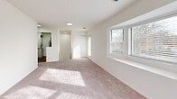 Located at 52 Greenview Circle in West Sayville, New York, this single-floor home offers a clean, well-maintained layout designed for comfortable everyday living. The interior is finished with neutral white walls and soft wall-to-wall carpeting throughout the living and bedroom areas, creating a bright and cohesive aesthetic across the entire space.

The main living area is generously proportioned, benefiting from multiple windows fitted with horizontal blinds that allow natural light to filter in while maintaining privacy. Recessed lighting supplements the natural light, keeping the space well-illuminated throughout the day. Views of mature trees and surrounding greenery are visible through the windows, lending the interior a calm, connected-to-nature quality.

The floor plan, as seen in the 3D model, reveals a practical and efficient layout that includes a kitchen with cabinetry and a sink, a separate living area, and additional rooms suitable for use as bedrooms. The kitchen is accessible from the main living space and features darker flooring that contrasts with the carpeted areas, clearly delineating functional zones. A closeted entry door provides a defined point of arrival.

Throughout the home, clean lines, consistent finishes, and an abundance of natural light contribute to an open and inviting atmosphere. The overall design prioritizes functionality and ease of use, making this West Sayville residence a straightforward and livable space.