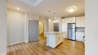 This well-appointed single-floor residence offers a thoughtfully designed open-concept layout that seamlessly connects the kitchen, dining, and living areas. The kitchen is a standout feature, showcasing crisp white shaker cabinets, granite countertops with subtle veining, and a full suite of stainless steel appliances including a refrigerator, range, microwave, and dishwasher. A central island with matching granite provides additional prep space and casual seating, while pendant lighting adds a refined touch overhead. Luxury vinyl plank flooring flows throughout the main living areas, offering both durability and a warm aesthetic. The living area benefits from natural light through vertical blinds and is complemented by a ceiling fan for added comfort. The bedroom is carpeted for a cozy feel, features a ceiling fan, and receives natural light through a window with blinds. The bathroom is finished with consistent granite countertops, white cabinetry, a large framed mirror, and accessibility grab bars, reflecting a practical and inclusive design. Neutral tones throughout the unit create a clean, move-in-ready atmosphere suited to a variety of interior styles.